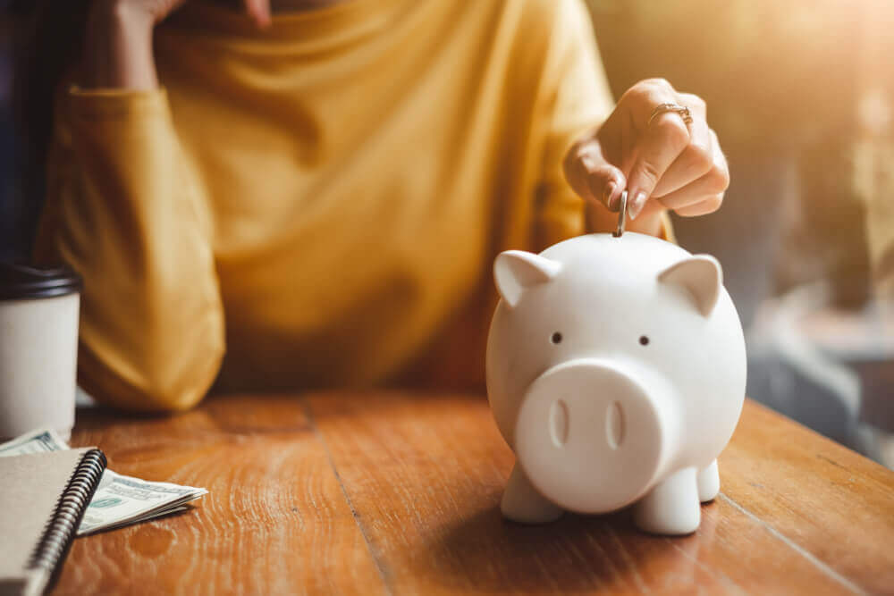 Woman putting coin in white piggy bank