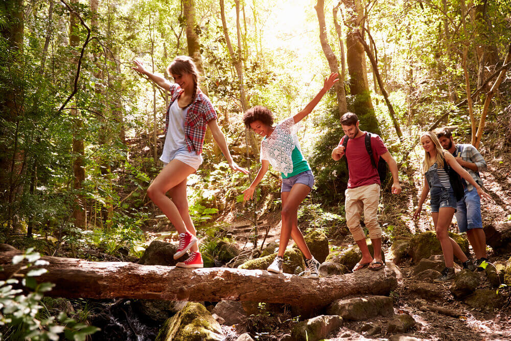 young adults hiking in forest, crossing stream on a log
