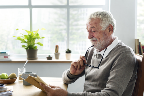 older man sitting in kitchen while reading a book